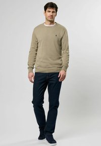 Beige pulóver ribbelt textúrával és kerek nyakkivágással, sötétkék farmernadrággal párosítva. A modellen tengerészkék sportcipő van.