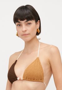 Gehaakte bikini top met een driehoekige vorm in bruin en tan kleuren, verfraaid met drie decoratieve kralen in het midden.