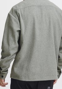 Grijs jack van een wolmix met een ontspannen pasvorm, lange mouwen, manchetten met knoopdetails en een licht gestructureerde afwerking. Heeft een naad in het rugpand.