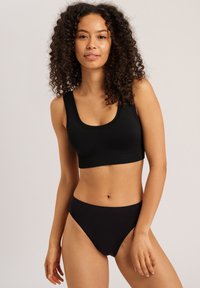 Sostenedor deportivo negro con tirantes anchos y escote en forma de scoop, combinado con bragas negras de talle alto. Tejido suave con una textura lisa.