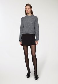 Maglione grigio lavorato a maglia, gonna avvolgente nera, collant trasparenti neri e scarpe ballerine in pelle verniciata nera. Il maglione ha maniche lunghe e scollo a giro.