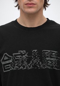 Gros plan d'une personne portant un t-shirt noir avec un motif abstrait blanc représentant un paysage urbain sur la poitrine.