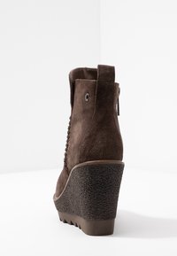 Bruna mocksneakers med kilklack och en texturerad svart plattform, med snörning och en ögla baktill för enkel påtagning.