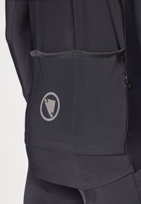 Mustmust värvi spordirõivas, millel on tagakott, sile tekstuur ja metalliline logo detail. Kujundatud funktsionaalsuseks ja mugavuseks.