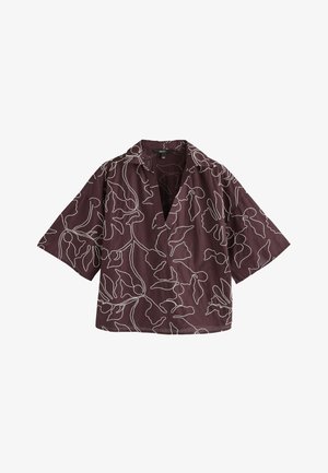 Blouse courte manches violet foncé avec motifs floraux abstraits blancs en lignes et col en V large et ouvert.