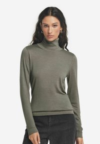 Grön polotröja tillverkad av mjukt material, med långa ärmar och en figurnära design, samt ribbat krage och fåll.