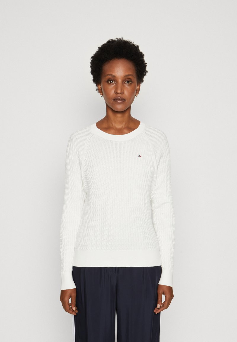 Maglione bianco a maglia con texture a coste, scollo rotondo e maniche lunghe. Presenta un piccolo logo sul petto e un orlo aderente.