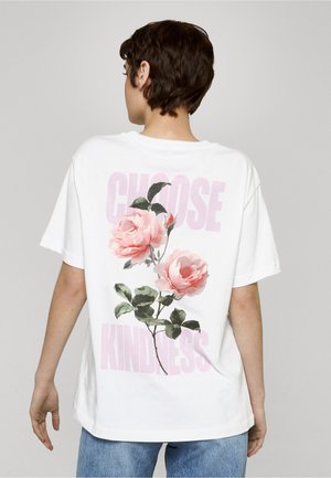 Biele bavlnené tričko s kvetinovou grafikou ružových ruží a textom "ZVOĽ SI Láskavosť" vo svetloružovej farbe, s voľným strihom.