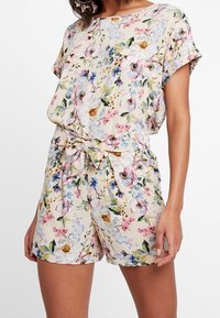 Blumiger Jumpsuit mit einem hellbeigen Hintergrund und pinken, blauen und gelben Blumen, kurzen Ärmeln und einer gebundenen Taillenpartie.