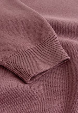 Pehmeast lilla kudumkangast kampsun, millel on soonikkoes mansett ja sile, tekstureeritud pind, ilma nähtavate mustrite või kaunistusteta.