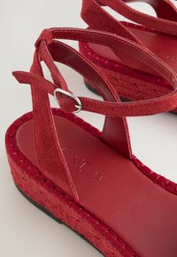 Rode suède wedge sandalen met kruislingse banden en een metalen gesp. Gevlochten jute details op de zool, gladde leren binnenzool, platte zwarte buitenzool.