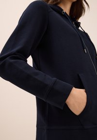 Sweatshirt à capuche bleu marine en tissu texturé, doté d'une fermeture éclair, d'une poche frontale et de poignets côtelés.