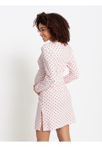Rosa långärmad klänning med svarta prickar. Har en figurnära design, sidklyftor och mjukt tyg, lämplig för en gravid figur.
