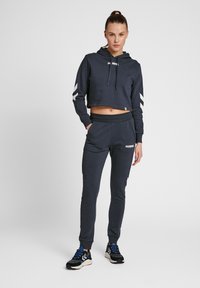 Mörkblå kort hoodie med dragsko, vit logotyp och chevron-accenter på ärmarna, i kombination med matchande joggers med elastisk midja.