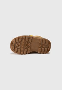 Semelle en caoutchouc marron avec un motif de marche texturé, arborant le logo "TOMMY HILFIGER". Le design comprend des rainures angulaires et des détails circulaires.