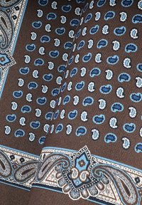 Brązowy materiał z powtarzającym się wzorem niebieskich kształtów paisley oraz ozdobnymi detalami w niebieskim i białym kolorze. Mięsista tekstura z tkaną strukturą.