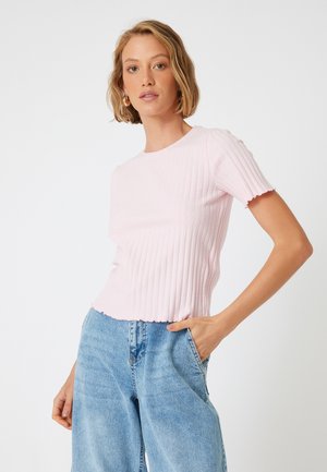 Lichtroze geribbelde gebreide top met korte mouwen, een ronde halslijn en een golvende zoom. Gecombineerd met high-waisted blauwe denim jeans.