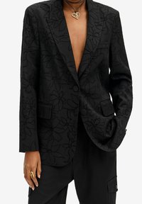 Schwarzer Blazer mit floralem Reliefmuster, strukturiertem Design, Reverskragen, Ein-Knopf-Verschluss und zwei Fronttaschen.