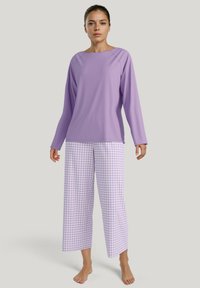 Lichtpaarse lange mouw top met brede halslijn, gecombineerd met lichtpaarse en witte geruite wijde broek. De stof lijkt zacht en glad te zijn.