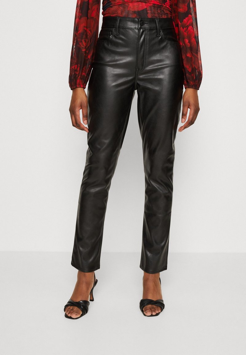 Pantalon en cuir noir avec une coupe slim, taille haute et texture lisse. Associé à des sandales à talons noires.
