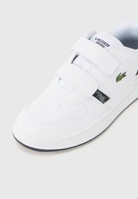 Λευκό αθλητικό παπούτσι με λουράκια βέλκρο, καουτσούκ σόλα, επάνω τμήμα από λείο δέρμα, με πράσινο κεντημένο λογότυπο και γεωμετρικό σχέδιο στολισμού.