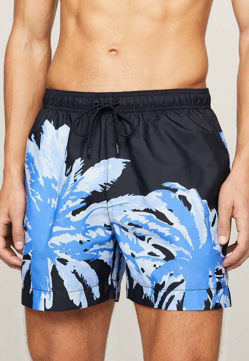 Costume da bagno neri con grandi motivi di foglie di palma blu. Vita elastica con cordino. Materiale leggero e ad asciugatura rapida.