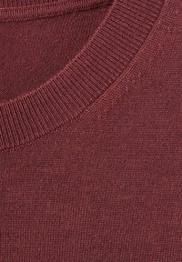 Burgundowy dzianinowy sweter z prążkowanym okrągłym dekoltem. Miękka tekstura i jednolity wzór ściegów na całej powierzchni. Widok z bliska.