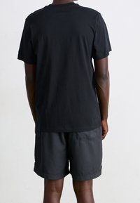 Camiseta de algodón negra con mangas cortas y cuello redondo, combinada con shorts negros de textura suave y bolsillos laterales.