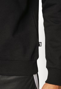 Felpa nera con polsini e orlo a coste, tessuto morbido, design minimalista. Include un piccolo etichetta di marca sul lato.