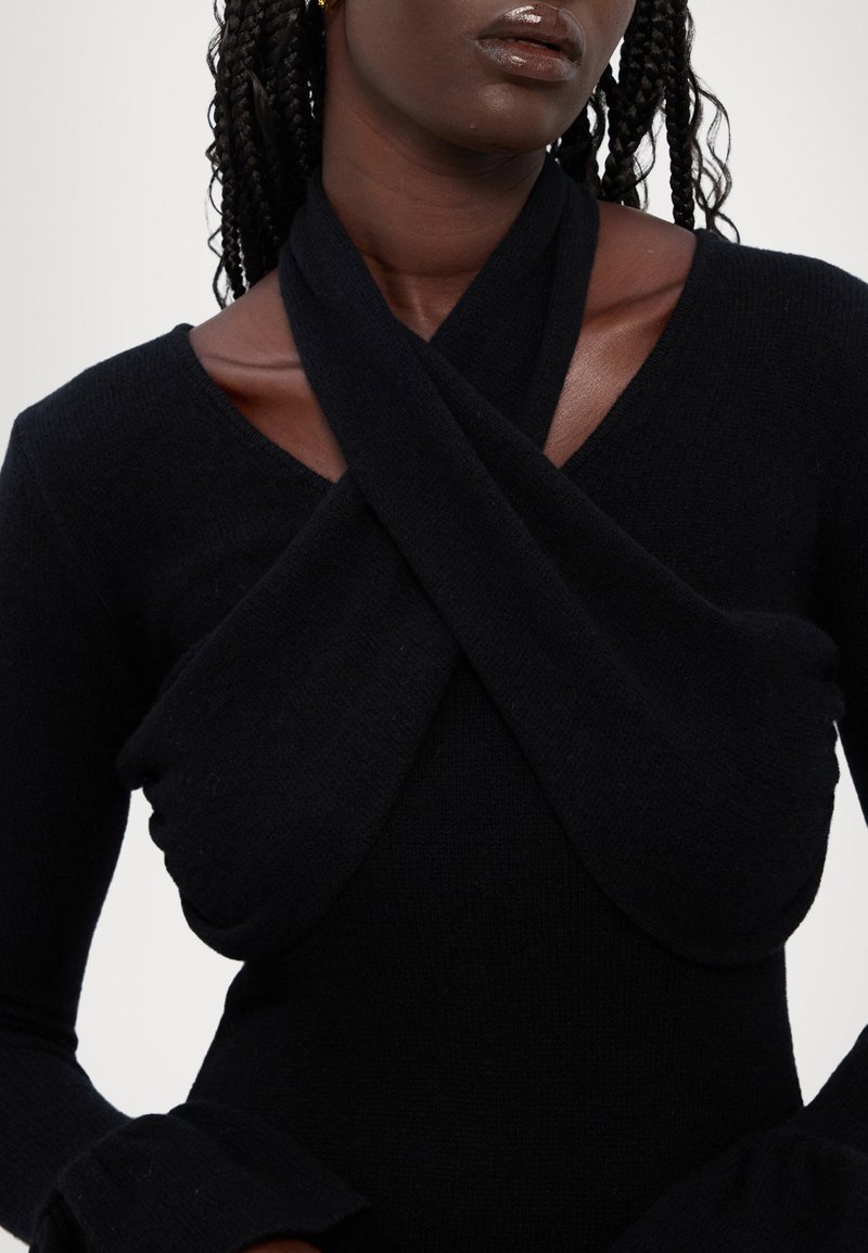 Top nero in maglia con un design incrociato al collo, maniche lunghe e polsini svasati. Texture liscia e silhouette aderente.