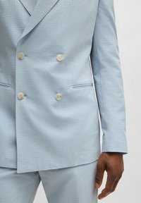 Ljusblå dubbelknäppt kavaj i texturerat tyg, med två stora krämfärgade knappar och sidofickor. Skräddarsydd passform.