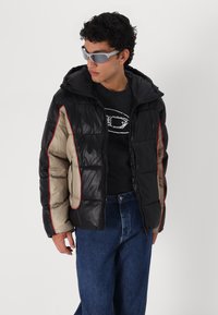 Casaco puffer com um design em bloco de cores preto e bege, realçado com costuras vermelhas, material texturizado e capuz.