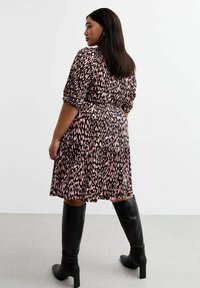 Musterkleid in Braun und Pink, mit taillierter Taille und schwingendem Rock, kurzen Ärmeln und plissierter Gestaltung. Kombiniert mit schwarzen Stiefeln bis über das Knie.