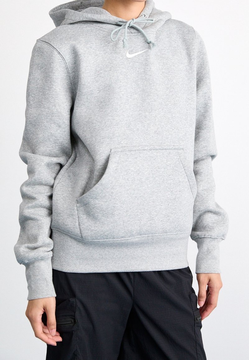 Grå bomullshoodie med känguruficka, justerbar dragsko i huvan och en liten vit Nike-logga på bröstet. Avslappnad passform och ribbade muddar.