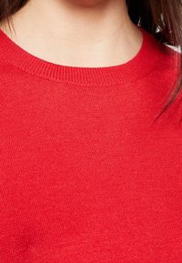 Czerwony sweter dzianinowy z okrągłym dekoltem. Tkanina ma gładką fakturę i ściągaczowy brzeg, co wskazuje na dopasowany krój.