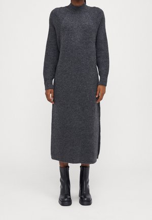 Dunkelgraues, langes Strickkleid mit langen Ärmeln, getragen mit schwarzen Stiefeletten an einer stehenden Person.