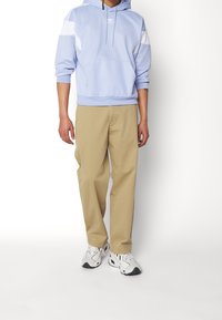 Ljusblå huvtröja med vita detaljer, beige byxor och vita sneakers med svarta detaljer. Slät väv, avslappnad passform och fickor.