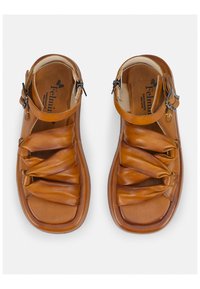 Sandalias de cuero marrón claro con un diseño trenzado en la parte superior, correa ajustable y una suela acolchada. Hechas a mano con costuras visibles.