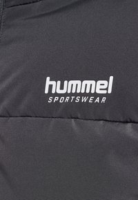 Giacca nera imbottita con una texture liscia, dotata di un logo "hummel" bianco e la scritta "SPORTSWEAR" sul davanti.
