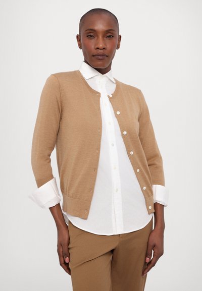 Beige cardigan with long sleeves, round neckline, and button closure, worn over a white collared shirt. Smooth texture, lightweight material.