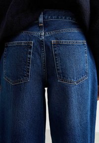 Jeans in denim blu con un taglio a gamba dritta, tasche posteriori distintive e cuciture gialle a contrasto lungo le cuciture.