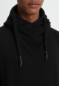 Felpa nera con cappuccio a scollo avvolgente, dotata di coulisse con punte in gomma, realizzata in tessuto morbido con texture liscia.