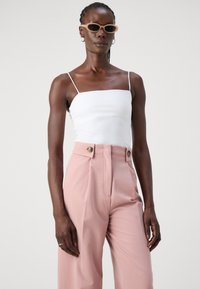 Hvit tettsittende cami med tynne stropper, kombinert med høyt liv, lyse rosa bukser med doble knapper. Solbriller med runde rammer.