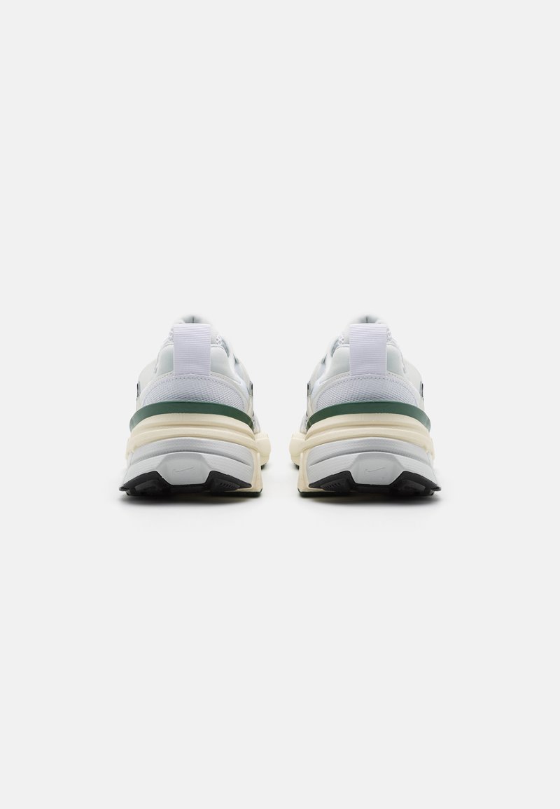 Zapatilla blanca con un diseño grueso, que presenta un acento verde y materiales texturizados. Suela de goma con un patrón de tracción negra.