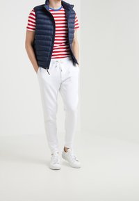 Námořnická prošívaná vesta přes červené a bílé pruhované tričko, spárovaná s bílými tepláky a bílými teniskami. Obsahuje zip a stahovací šňůrky.