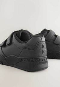 Schwarze Sportschuhe mit Klettverschlüssen, strukturierten Obermaterialien, einer dicken Gummisohle und einem gemusterten Fersendetail. Robustes, funktionales Design.