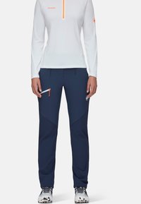 Vit långärmad topp med orange detaljer, tillsammans med marinblå byxor med sidfickor och en smal passform. Strukturerad, sportig design.