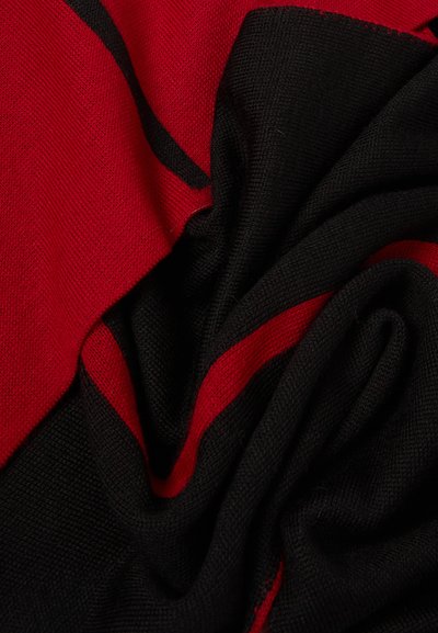 Gros plan d'un tissu tricoté doux avec de larges rayures rouges et noires torsadées pour montrer la texture et le contraste des couleurs.