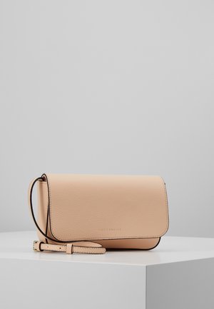 Bolso bandolera de cuero beige con cierre de solapa y correa ajustable, descansando sobre un pedestal blanco contra un fondo gris.