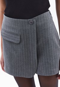 Shorts en chevron gris fabriqués dans un tissu à texture subtile. Comprend une poche unique et une fermeture à bouton à la taille.